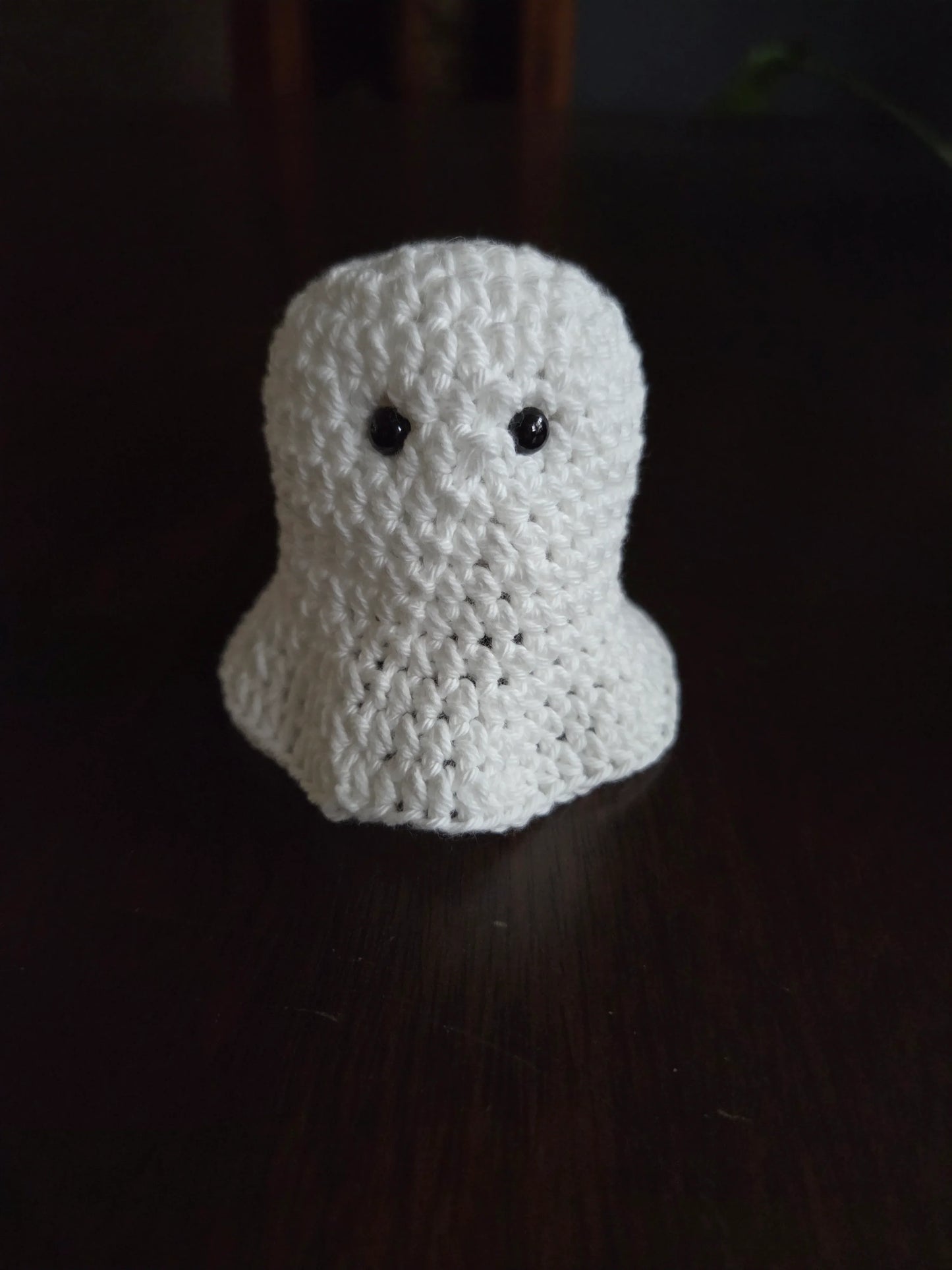 Handmade crochet ghost amigurumi with black eyes on a dark wooden surface