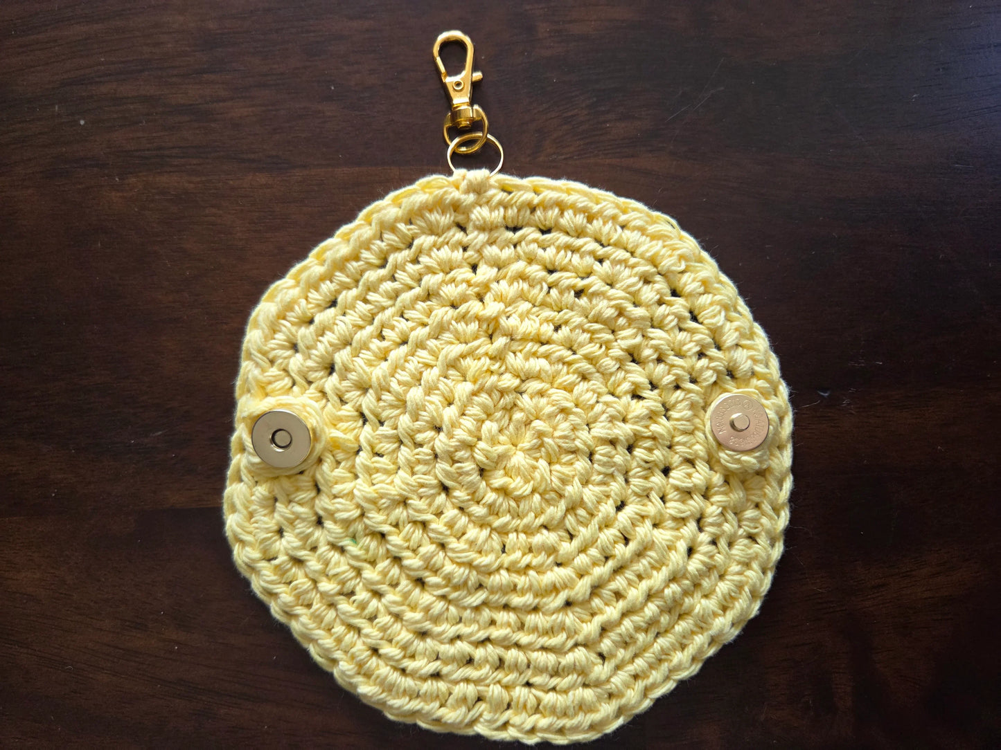 Yellow crocheted round keychain pouch with metal clasp and snap buttons on wood table