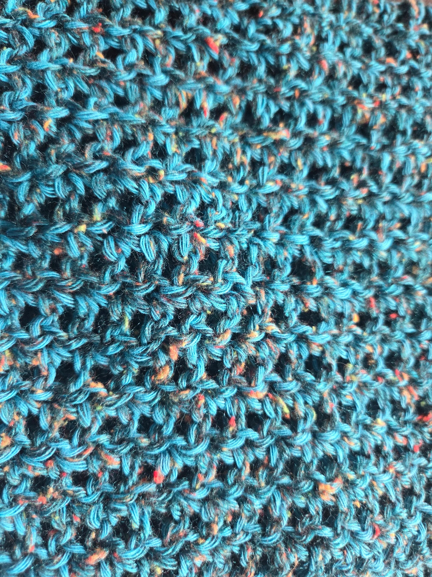 Close-up of blue crochet fabric with colorful speckles and textured yarn pattern