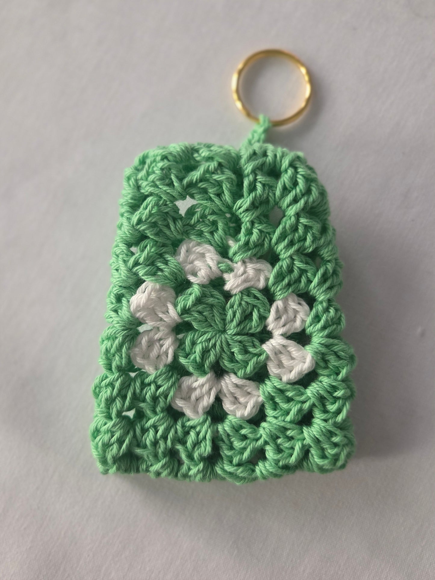 Green and white crochet keychain with granny square pattern on white background