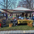 Handmade craft market booth displaying crochet items, framed art, and cozy gifts outdoors.