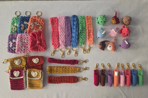 Handmade crochet keychains, wristlets, and pouches in colorful yarn on a light background.