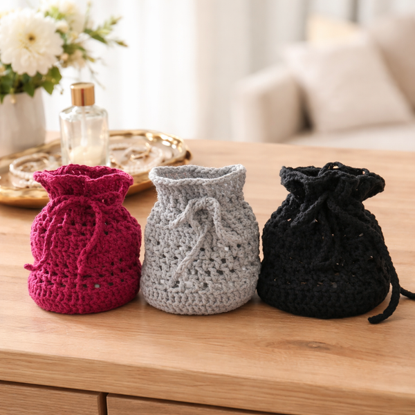 Handmade crochet gift pouches in pink, gray, and black on wooden table