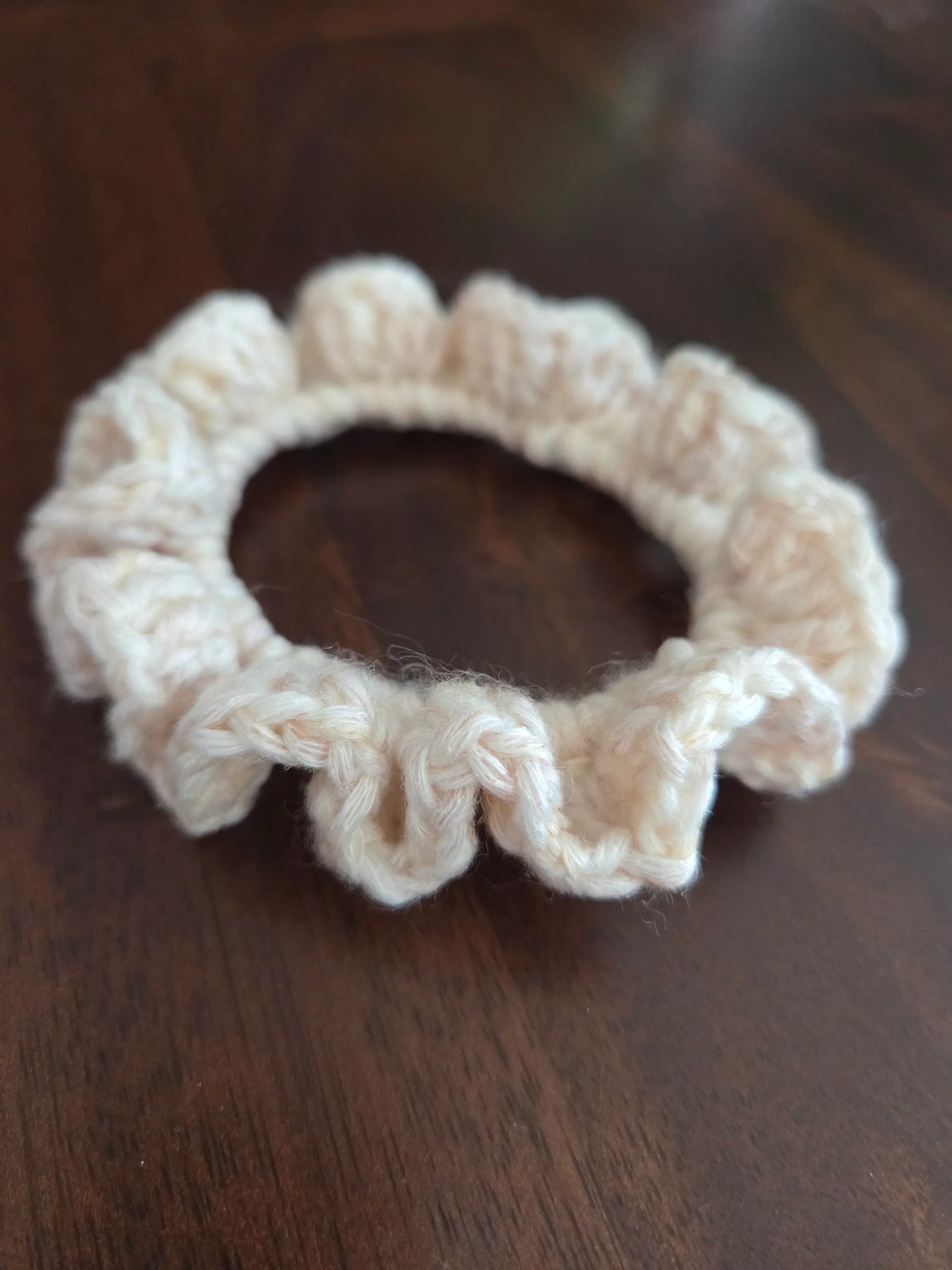 Beige crochet scrunchie with ruffled edges on dark wooden surface