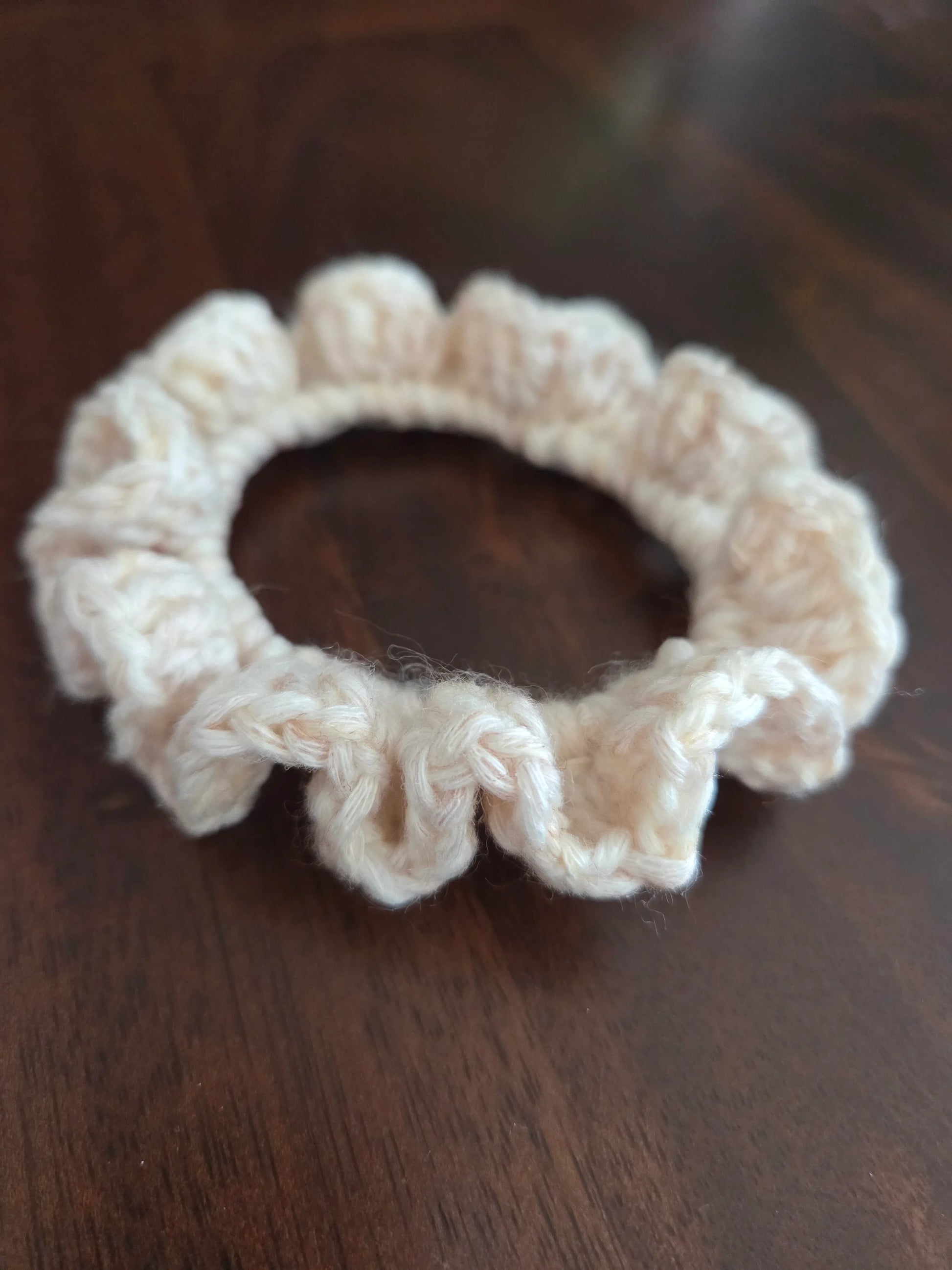 Beige crochet scrunchie with ruffled edges on dark wooden surface