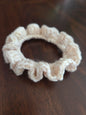 Beige crochet scrunchie with ruffled edges on dark wooden surface