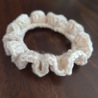 Beige crochet scrunchie with ruffled edges on dark wooden surface