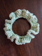 Handmade light green crochet scrunchie on a dark wooden surface