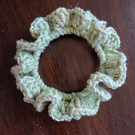 Handmade light green crochet scrunchie on a dark wooden surface