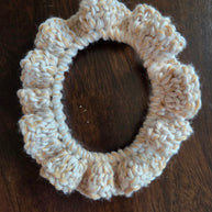 Beige handmade crochet scrunchie on dark wood surface