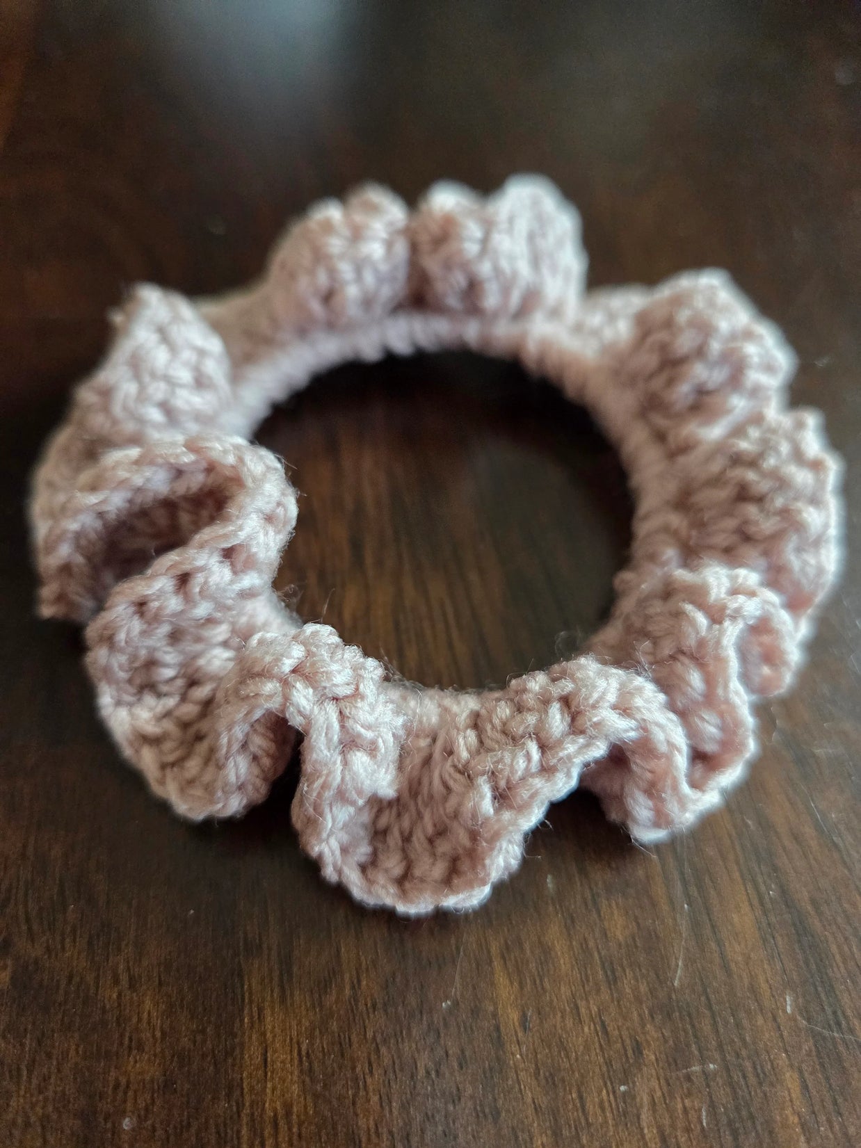 Pink crochet ruffle scrunchie on dark wooden surface