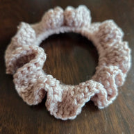 Pink crochet ruffle scrunchie on dark wooden surface