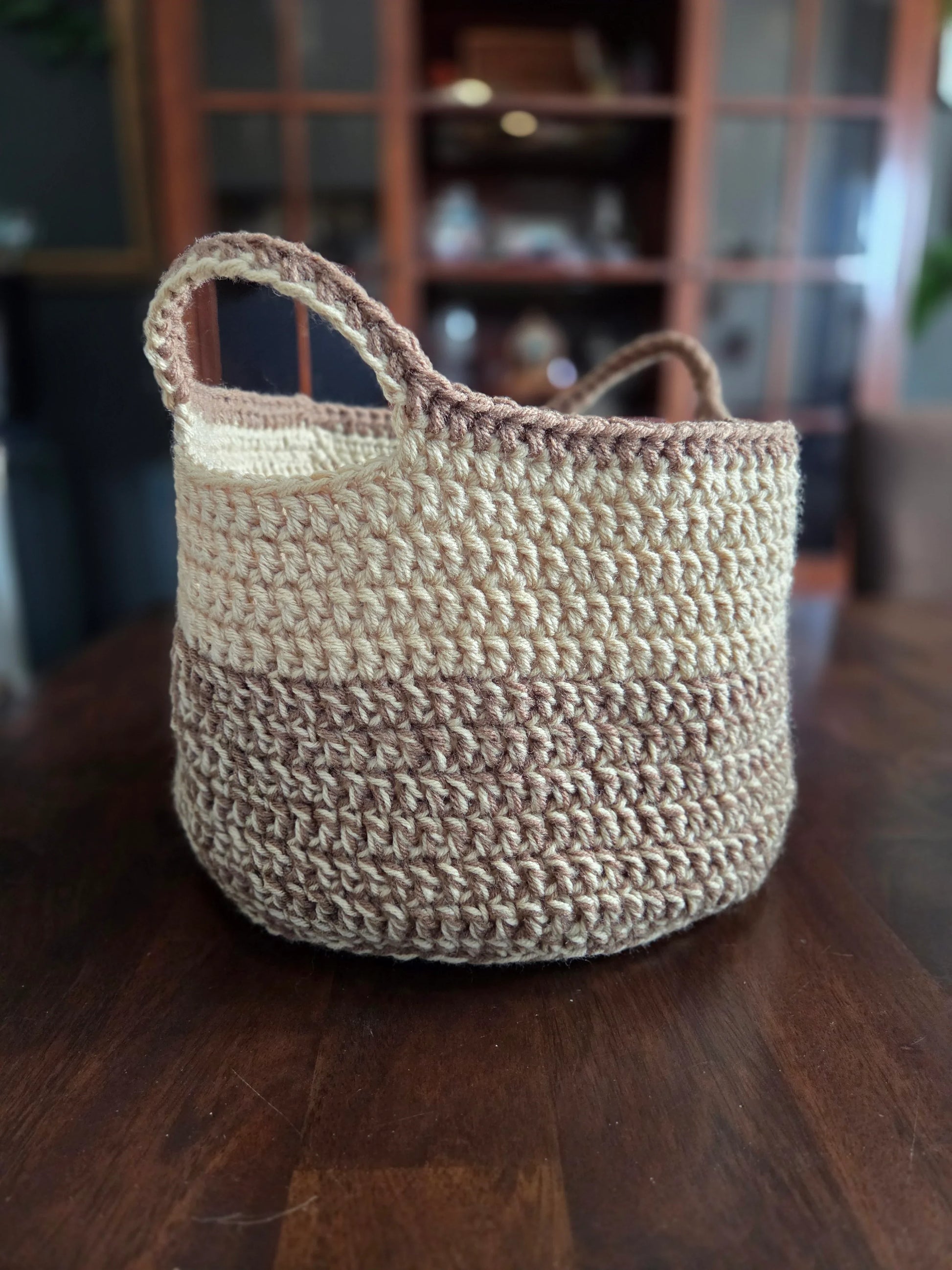 Handmade crochet storage basket with beige and brown yarn on a wooden table