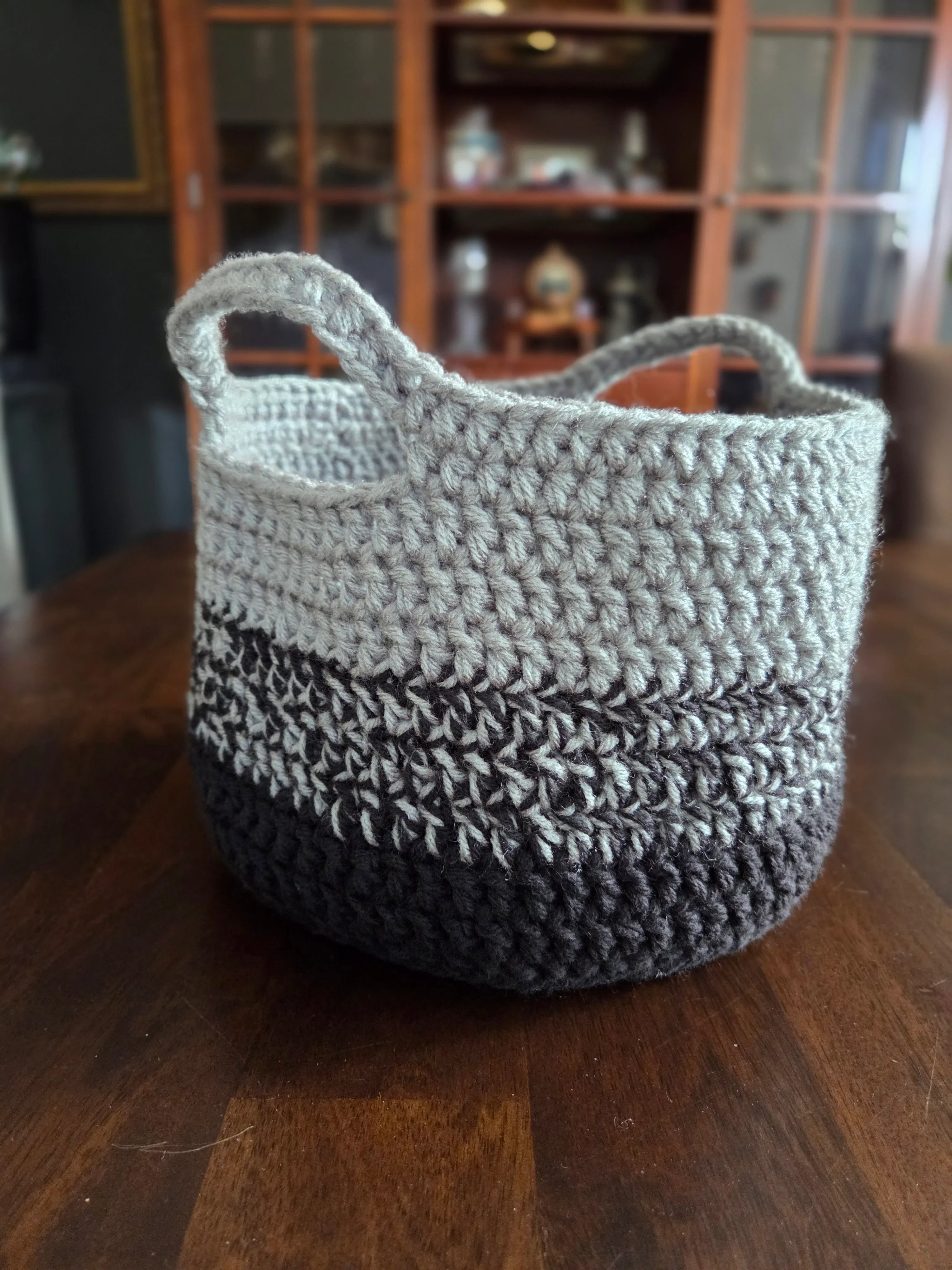 Handmade crochet basket with gray and dark yarn on a wooden table, home decor