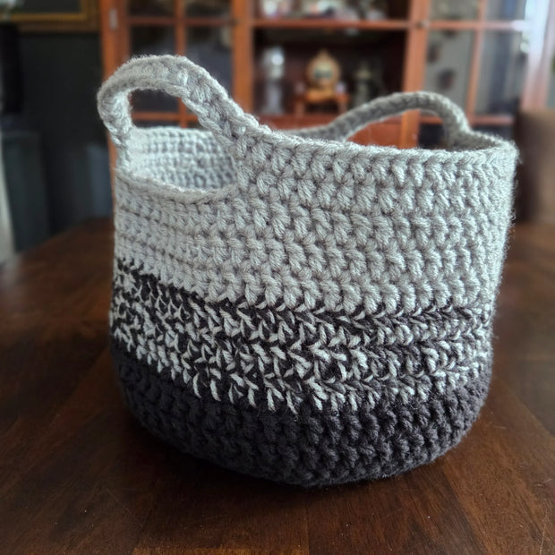Handmade crochet basket with gray and dark yarn on a wooden table, home decor