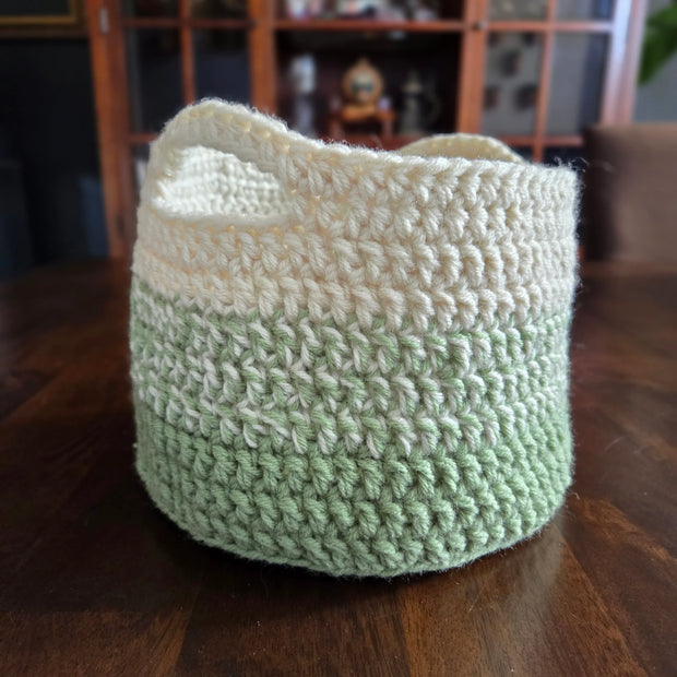 Handmade green and cream crochet basket on a wooden table, home decor storage.