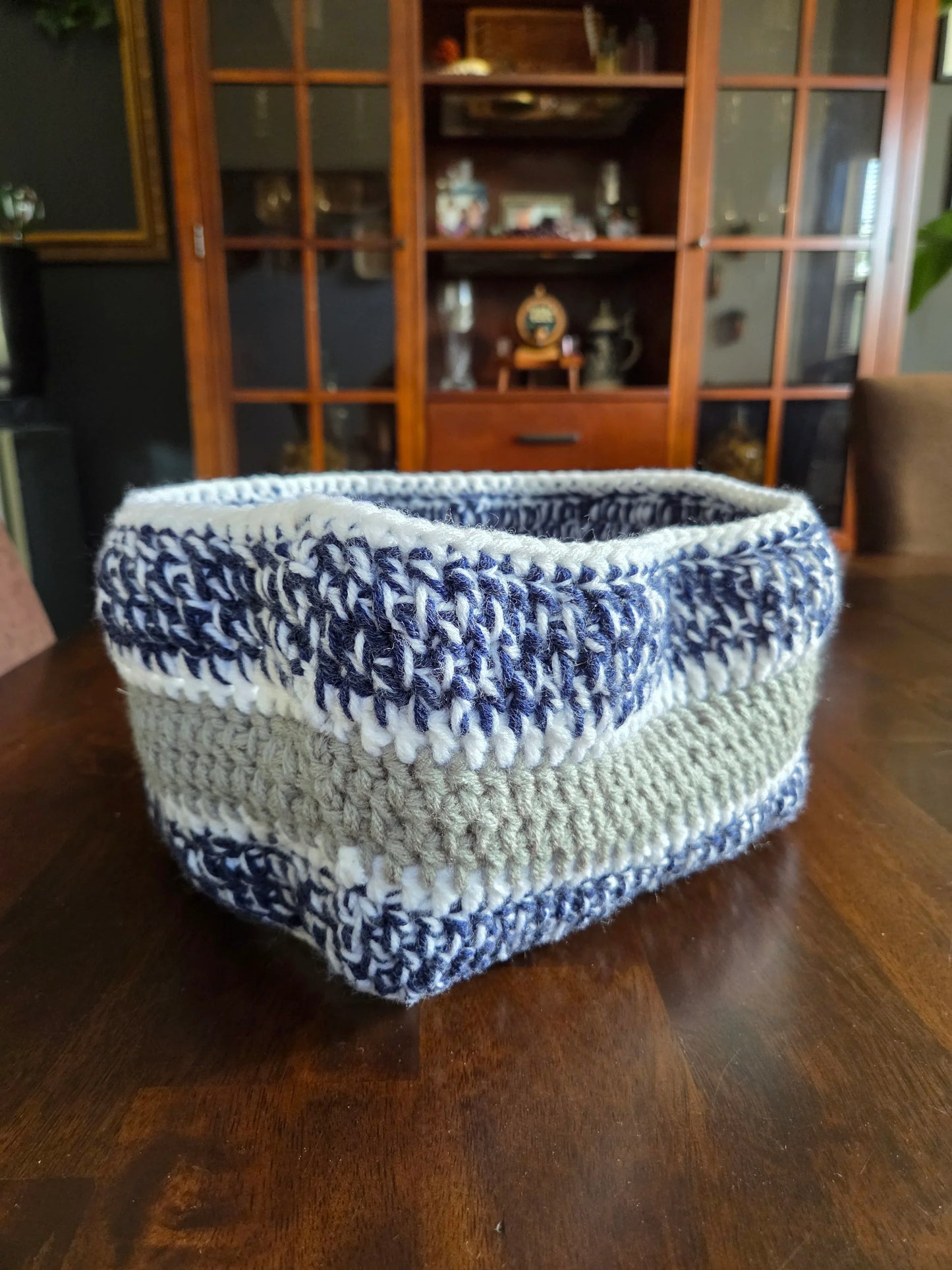 Handmade crocheted storage basket with blue, white, and beige yarn on wooden table
