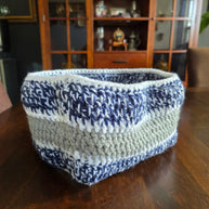 Handmade crocheted storage basket with blue, white, and beige yarn on wooden table