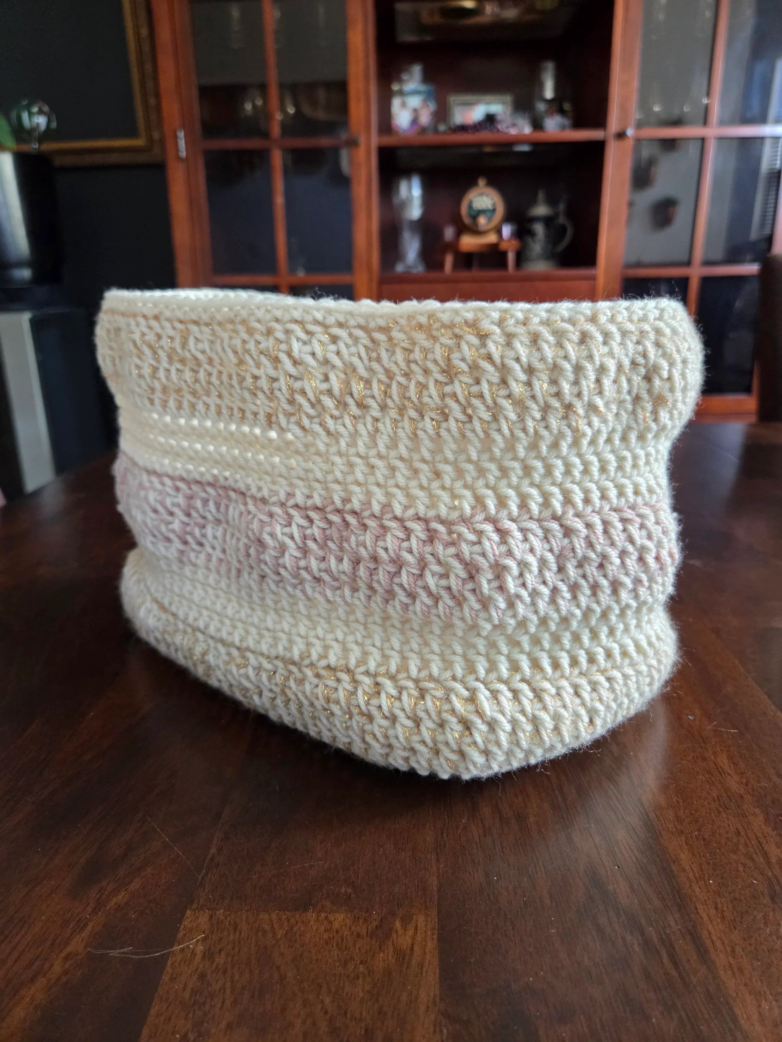 Handmade crochet basket with cream and pink yarn on wooden table