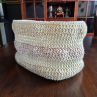 Handmade crochet basket with cream and pink yarn on wooden table