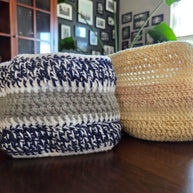 Handmade crochet baskets in blue, white, gray, and beige on a wooden table in a cozy room.