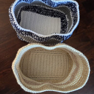 Two crochet storage baskets, one beige and one blue-white, on a dark wooden floor