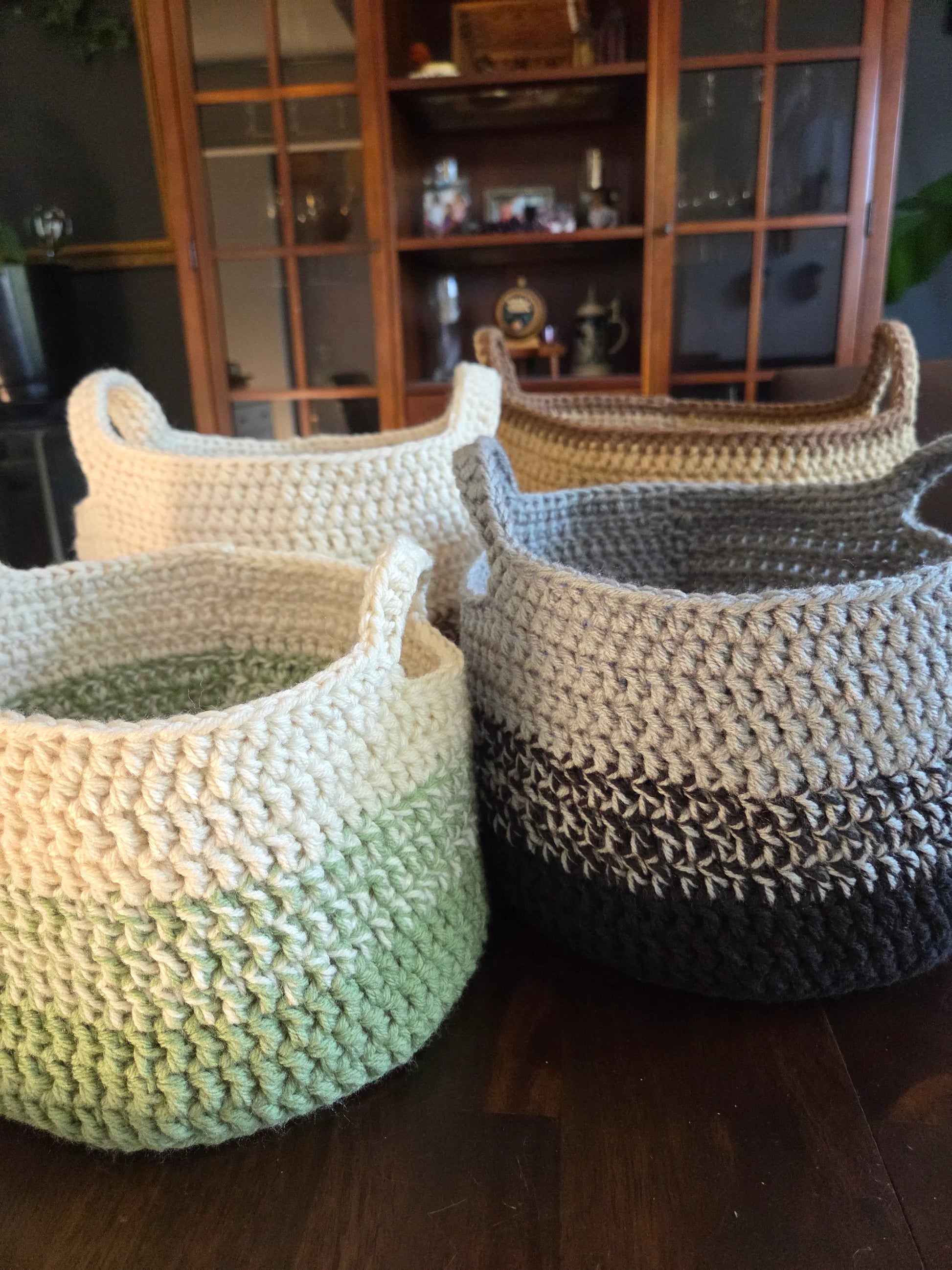 Handmade crochet baskets in neutral and green tones on a wooden table.