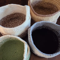 Set of four hand-crocheted storage baskets in natural colors on wooden surface