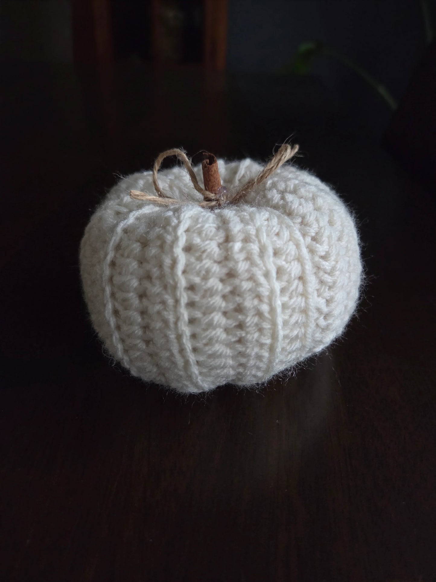 Handmade white knitted pumpkin with cinnamon stick stem on dark wooden table