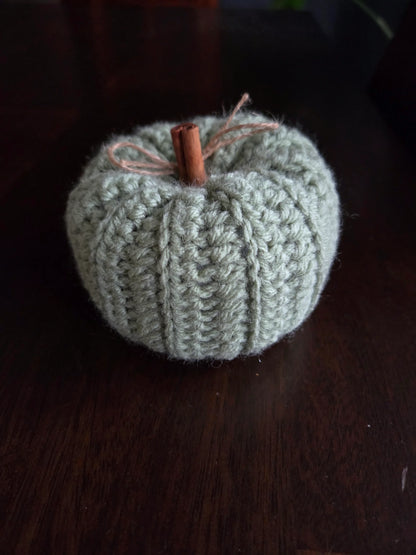 Handmade crochet pumpkin with cinnamon stick stem and twine bow on a dark wood table