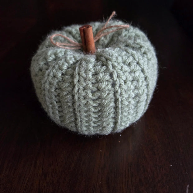 Handmade crochet pumpkin with cinnamon stick stem and twine bow on a dark wood table