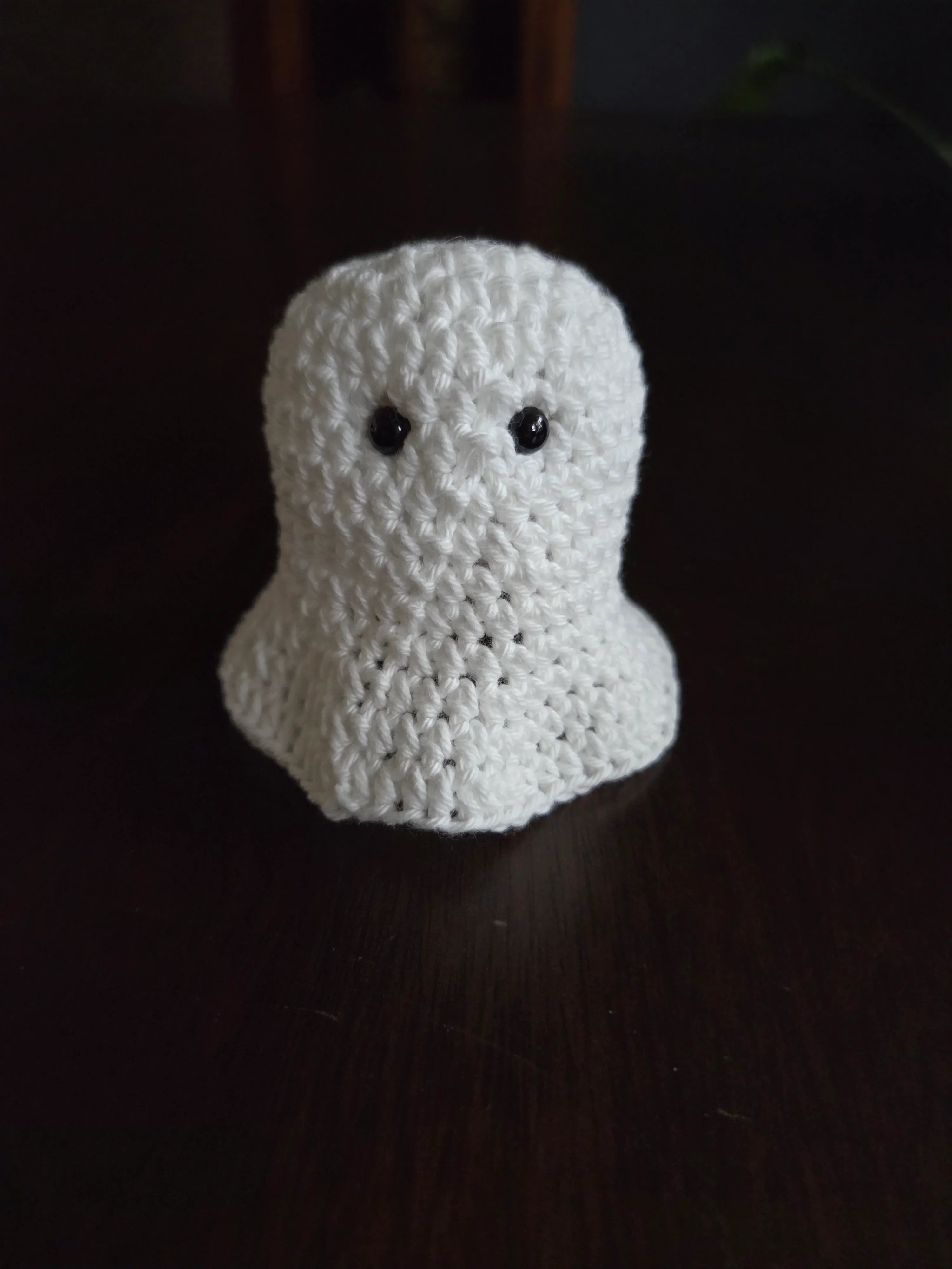 Handmade crochet ghost amigurumi with black eyes on a dark wooden surface