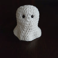 Handmade crochet ghost amigurumi with black eyes on a dark wooden surface