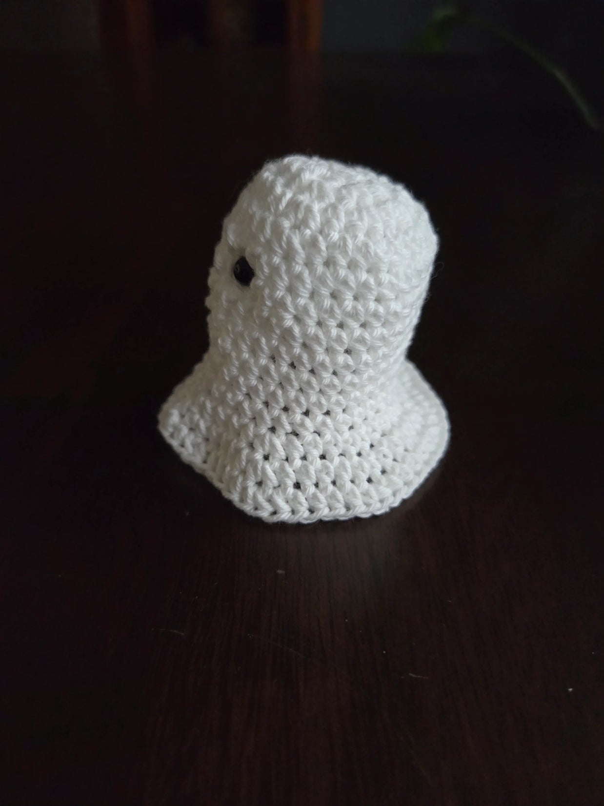 Handmade crochet ghost plushie on dark wooden table