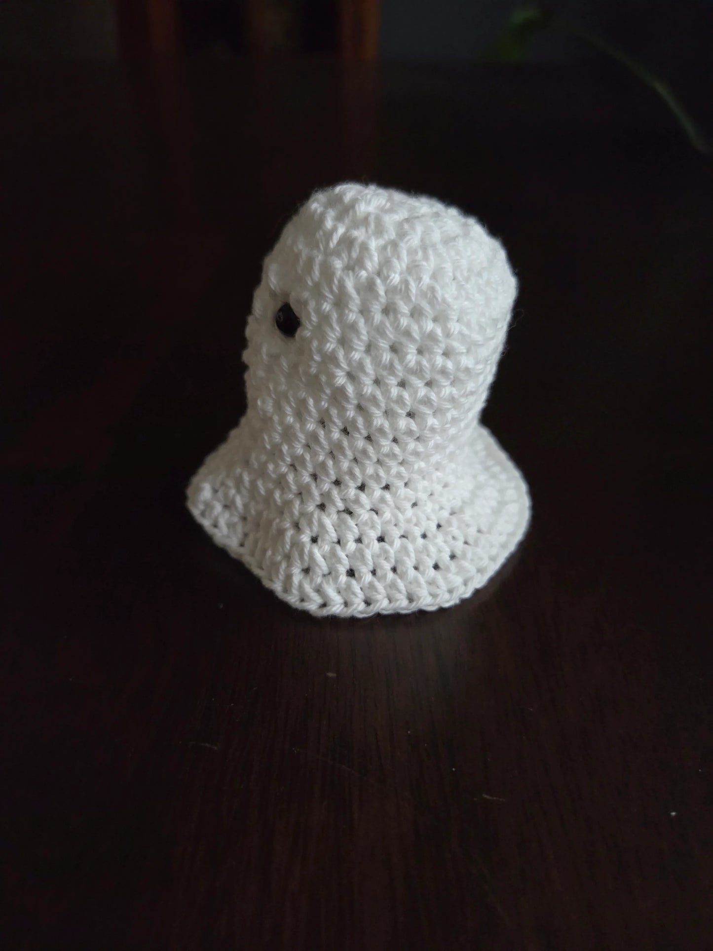Handmade crochet ghost plushie on dark wooden table
