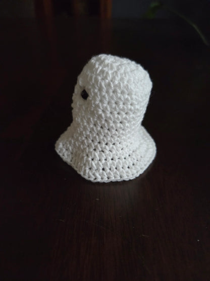Handmade crochet ghost plushie on dark wooden table