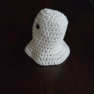 Handmade crochet ghost plushie on dark wooden table