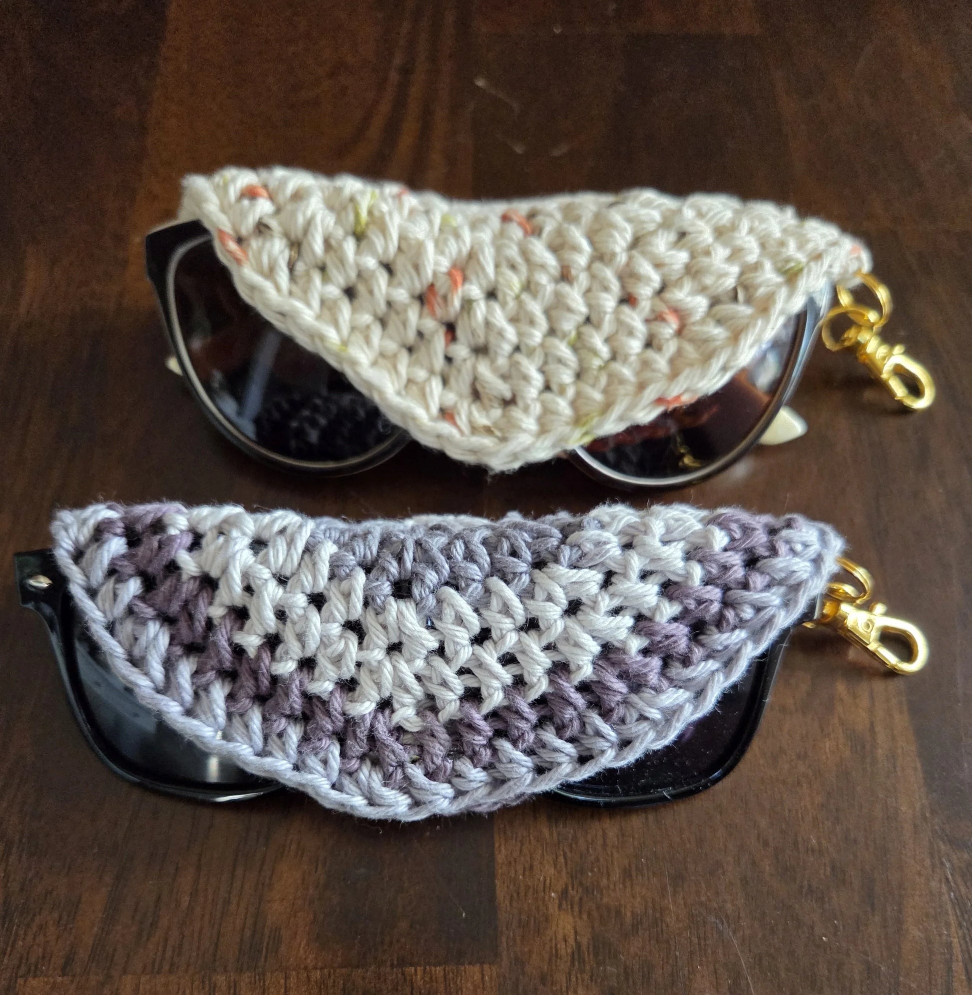 Two sunglasses with crochet half-moon cases and gold clips on a wooden surface