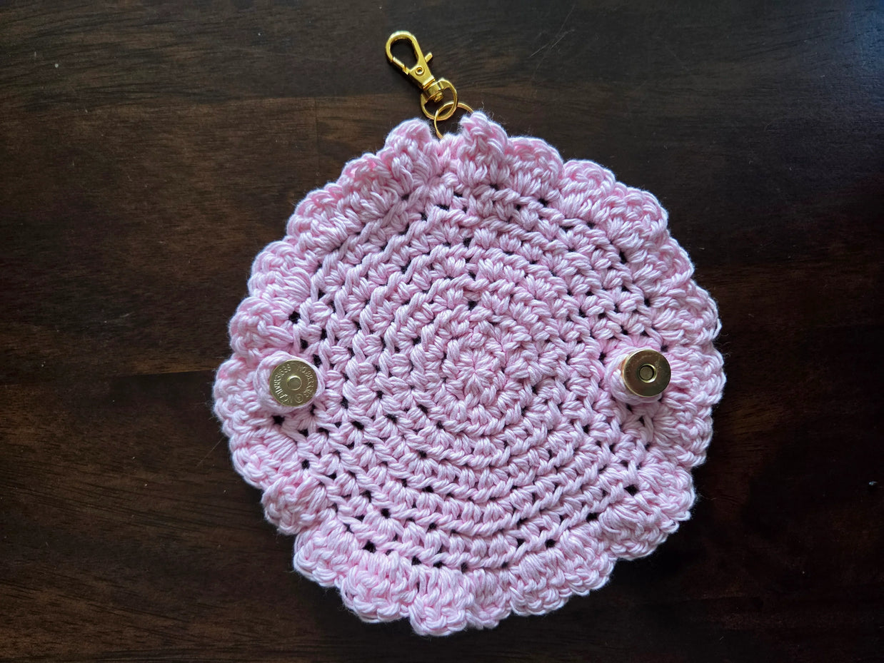 Pink crocheted keychain pouch with scalloped edges and metallic snap buttons on dark wood background