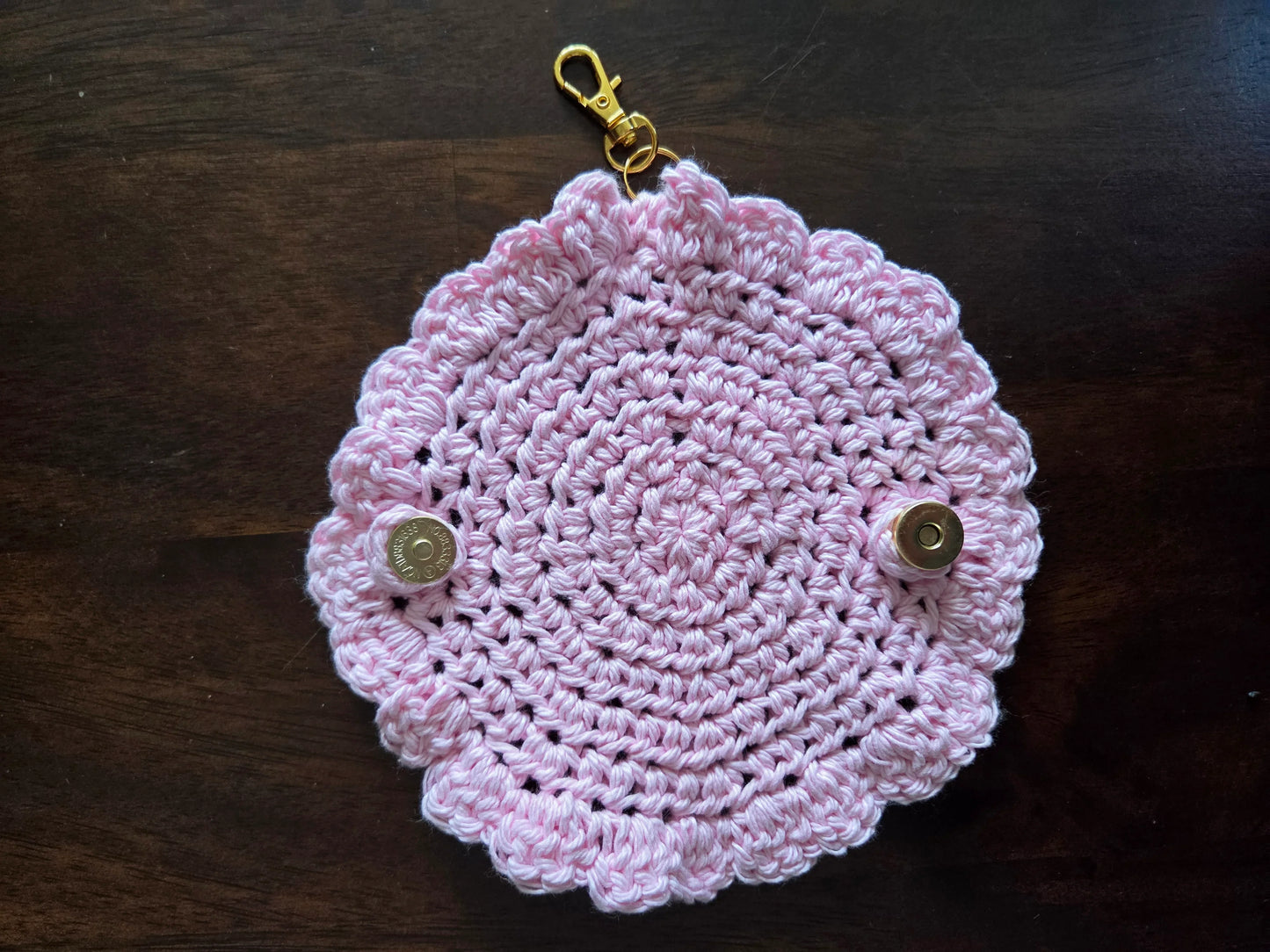Pink crocheted keychain pouch with scalloped edges and metallic snap buttons on dark wood background