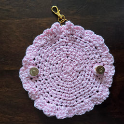 Pink crocheted keychain pouch with scalloped edges and metallic snap buttons on dark wood background