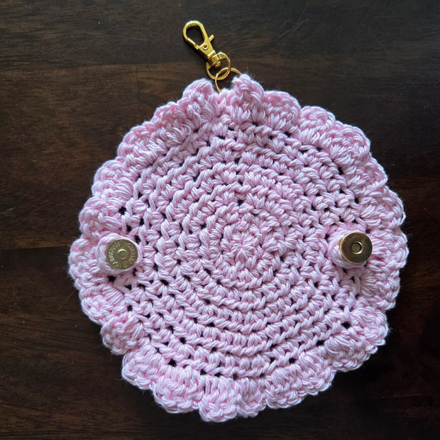 Pink crocheted keychain pouch with scalloped edges and metallic snap buttons on dark wood background