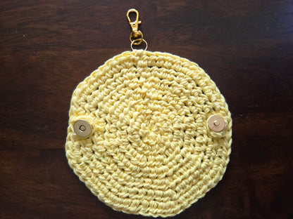 Yellow crocheted round keychain pouch with metal clasp and snap buttons on wood table