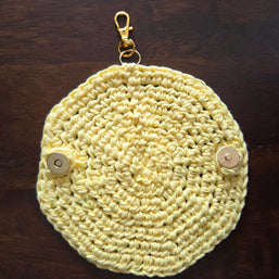 Yellow crocheted round keychain pouch with metal clasp and snap buttons on wood table