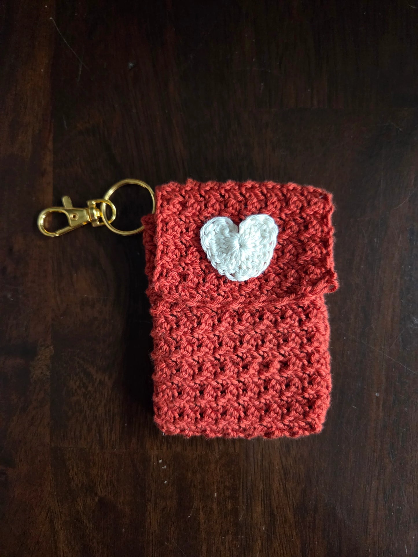 Handmade red crochet keychain pouch with white heart applique on dark wood background