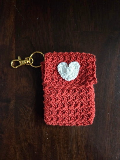 Handmade red crochet keychain pouch with white heart applique on dark wood background