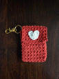 Handmade red crochet keychain pouch with white heart applique on dark wood background
