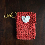 Handmade red crochet keychain pouch with white heart applique on dark wood background