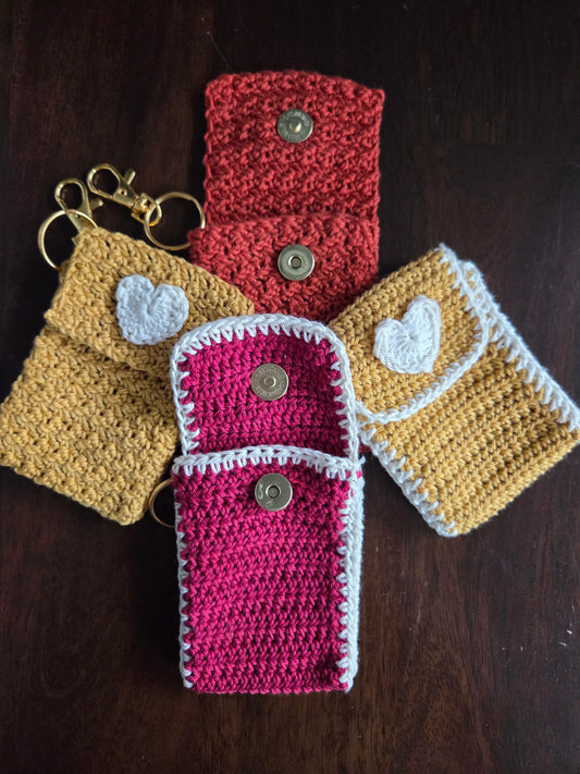 Handmade crochet keychain pouches with heart appliques and snap closures on wooden surface