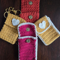 Handmade crochet keychain pouches with heart appliques and snap closures on wooden surface